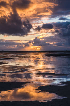 Sunset on a cloudy colorful sky over the North Sea in Denmark with high reflection in the water, verticalの写真素材
