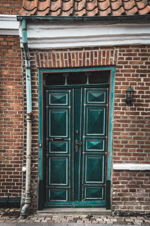 Old green warped crooked wooden door on a brick buildingの写真素材