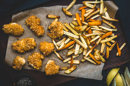 Homemade chicken nuggets with vegetable fries on black background, top view
