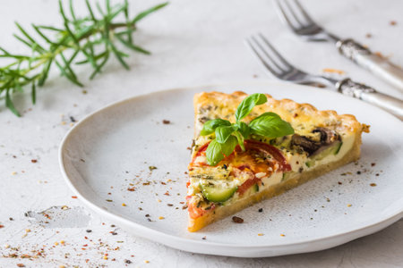 Piece of vegetable tart with mushrooms, tomatoes and zucchini on white backgroundの写真素材