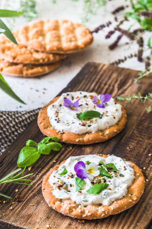Round crispbread with herbal cream cheese and fresh herbs on a wooden board, verticalの写真素材