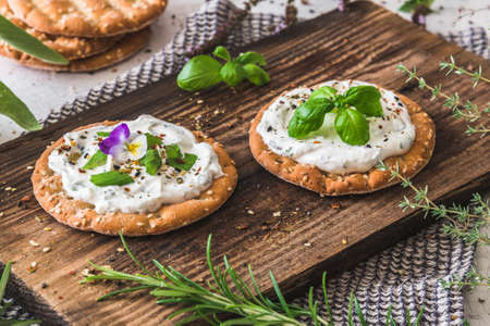 Round crispbread with herbal cream cheese and fresh herbs on a wooden boardの写真素材