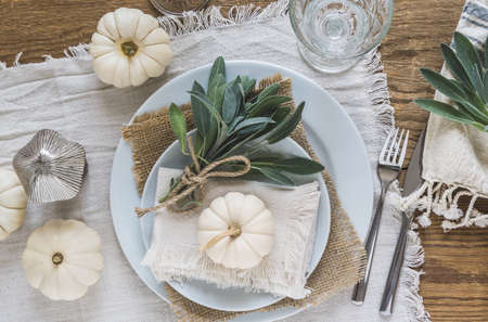 Place setting on a wooden table with white mini pumpkins, sage leaves and crystal glasses, decorated for Thanksgiving Day or Halloween, top view.の写真素材