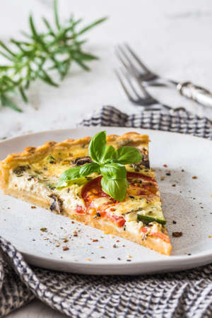 Piece of vegetable tart with mushrooms, tomatoes and zucchini on white background, verticalの写真素材