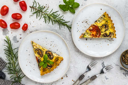 Two pieces of homemade vegetable tart with mushrooms, tomatoes and zucchini on white background, decorated with herbs, top viewの写真素材