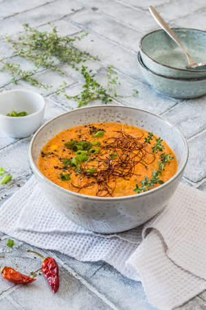 Tomato vegetable cream soup with chili, spring onions and fresh herbs on gray background, verticalの写真素材