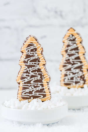 Two cookies shaped as christmas trees with chocolate and sugar glaze in bowls with coarse sugar on white background, vertical with copy spaceの写真素材