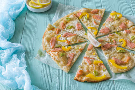 Tarte flambee with salmon, yellow pepper and spring onions on light blue backgroundの写真素材