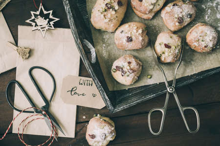 Mini stollen with sugar icing on a wooden tray, paper bags, scissors and gift ribbon on dark wood, scene for preparing advent or christmas gifts, top viewの写真素材