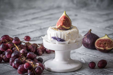 Whole round soft cheese with honey and fig on gray tiles, decorated with dark red grapesの写真素材