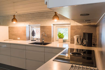 Modern kitchenette with white worktop, black sink and coppery metal lamps in industrial styleの写真素材