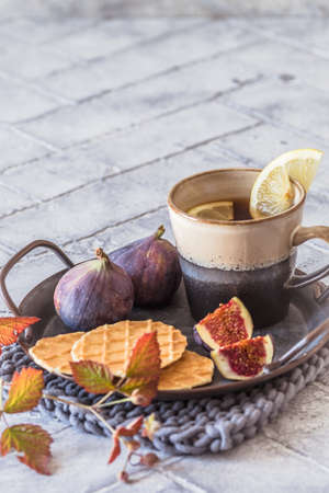 Cup of tea with cookies and fresh figs on a metal tray on gray tiles, verticalの写真素材
