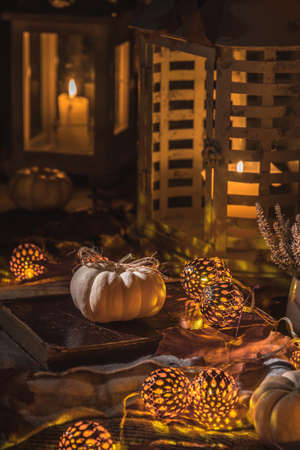 Autumn decoration with white pumpkins, lights, blanket and dried leaves on a terrace or patio in night, vertical stock photoの写真素材