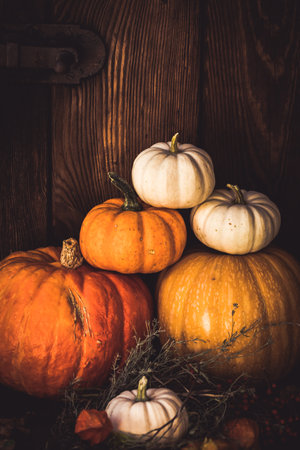 Stacked pumpkins of different sizes and colors with autumn decorations in front of a wooden wall, vertical with copy spaceの写真素材