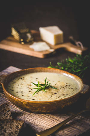 Bowl of parmesan cheese soup with rosemary on wooden background, vertical with copy spaceの写真素材