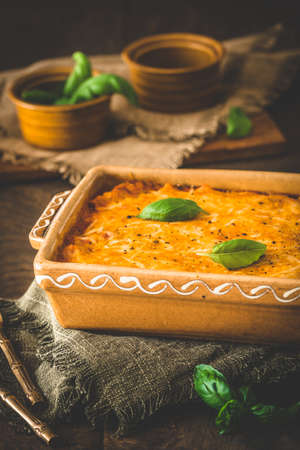 Gratin with fusilli pasta, tomato sauce, basil and cheese on wooden background, verticalの写真素材