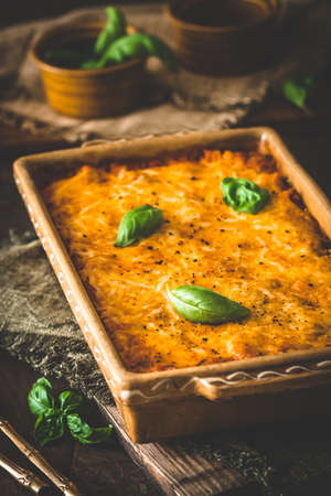 Pasta and cheese bake with tomato sauce and basil on wooden background, verticalの写真素材
