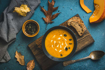 Blue bowl with pumpkin soup on a rustic wooden board on blue background, autumn leaves and colors, top viewの写真素材
