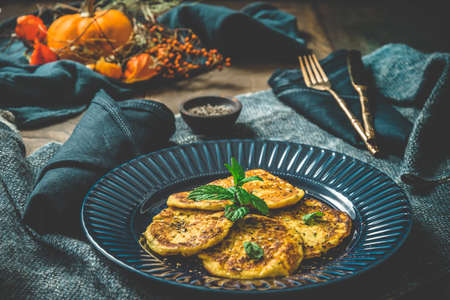 Small pumpkin pancakes with herbs on a blue plate on blue and wooden backgroundの写真素材