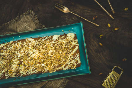 Cake with white chocolate, nuts, almonds and pistachios as a topping on wooden background, top view.の写真素材