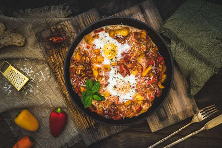 Shakshuka in an iron pan on wooden background. Middle eastern traditional dish. Fried eggs with tomatoes, bell pepper, vegetables and herbs. Top view.の写真素材