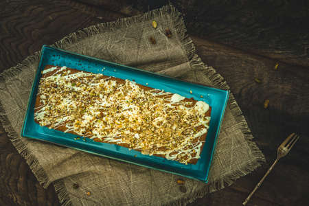 Cake with white chocolate, nuts, almonds and pistachios as a topping on wooden background, top view.の写真素材