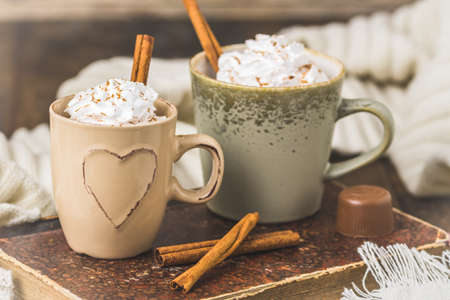 Two cups of coffee or hot chocolate with cream and cinnamon on an old book on wooden backgroundの写真素材
