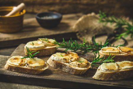 Baguette bread slices baked with goat cheese and honey, decorated with rosemaryの写真素材