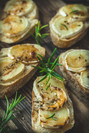 Baguette bread slices baked with goat cheese and honey, decorated with rosemary, on wooden background, vertical closeupの写真素材