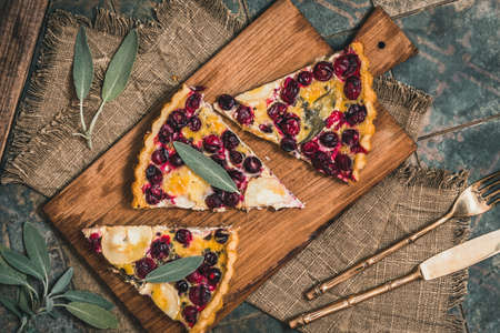 Pieces of a cranberry goat cheese tart with sage on rustic background, top view