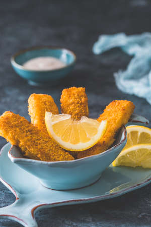 Fish fingers with lemon and sour cream on a blue background, verticalの写真素材