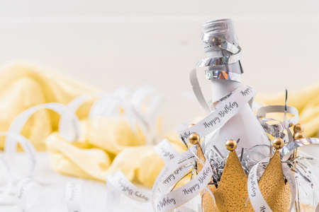 Small white bottle with sparkling wine in a decorative golden metal crown, decorated by streamers with text Happy Birthday. Close up with copy space.の写真素材