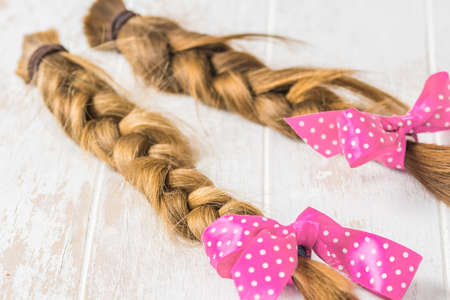 Two braids with pink ribbon on a white background, cut for wig donationの写真素材