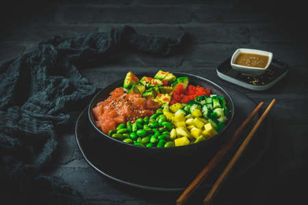 Japanese poke or buddha bowl with salmon, avocado, roe, mango, pies and cucumber in a black bowl on black backgroundの写真素材