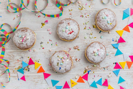Krapfen, Berliner or donuts with streamers, confetti and mini marshmallows on white wooden background. Colorful carnival or birthday image, top viewの写真素材