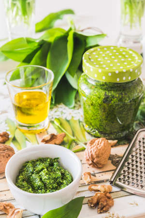 Homemade wild garlic pesto in a white bowl and its ingredients on a tray on white background, verticalの写真素材