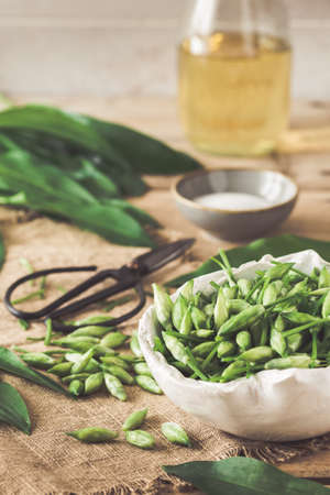 Wild garlic buds and leaves, salt and vinegar on a rustic wooden background, vertical. Preparation for canning.の写真素材