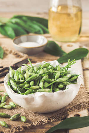 Wild garlic buds and leaves, salt and vinegar on a rustic wooden background, vertical. Preparation for canning.の写真素材