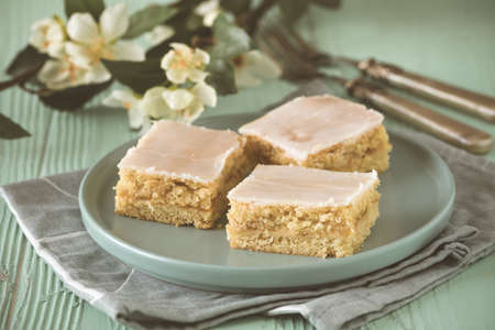 Pieces of covered apple pie with sugar icing on a light green background, decorated with flowering branchの写真素材