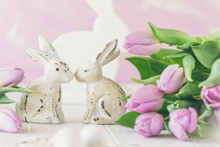 Two white wooden Easter bunnies surrounded by fresh pink tulips, pink backgroundの写真素材