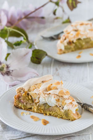 Pieces of rhubarb pie with meringue topping and almonds on white wooden background, verticalの写真素材