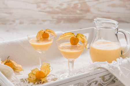 Two glasses and a carafe with eggnog and physalis fruits on a white wooden tray on a white marble backgroundの写真素材