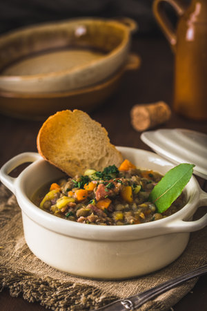 Bowl of lentil stew, toasted bread and bay leaf on rustic wooden table, verticalの写真素材