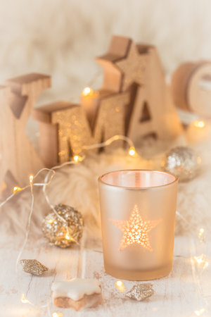 Small glass with tea light and word xmas in wooden capital letters, christmas decoration, and fairy lights on a white wood and white fur, verticalの写真素材
