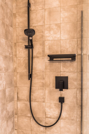 Black matte metal shower faucet on sand colored modern tiles, contemporary bathroom concept, verticalの写真素材