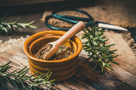 Dried herbs in a small bowl and fresh rosemary on rustic wooden backgroundの写真素材