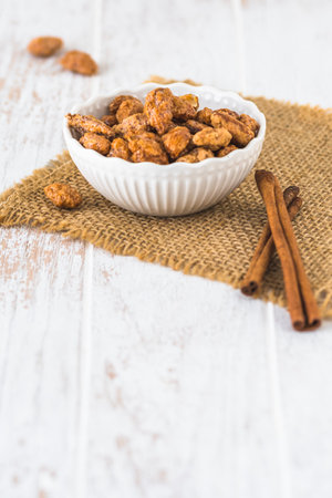 Bowl of sweet candied almonds on white rustic wooden background, vertical with copy spaceの写真素材