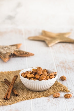 Bowl of sweet candied almonds on white rustic wooden background, wooden stars in the background, christmas decoration, vertical with copy spaceの写真素材