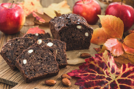 Autumn or christmas fruit cake with apples on a wooden board, decorated with colored leavesの写真素材