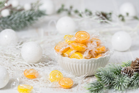 Bowl with candies in the form of orange and lemon slices, individually wrapped in foil, on white background with christmas decorationの写真素材
